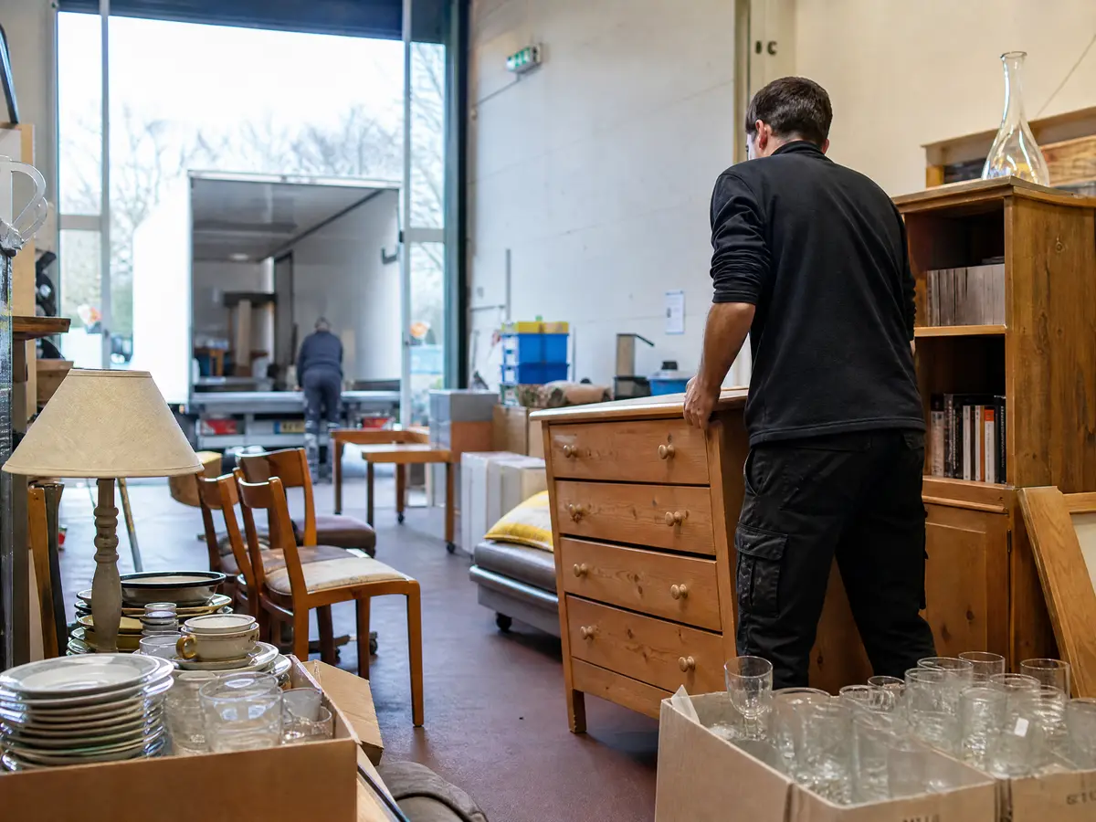 Crew member sets a good wooden chest of drawers among reusable furniture in a second-hand shop